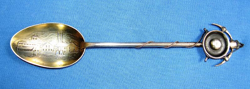 Souvenir Mining Spoon Lead SD.JPG - SOUVENIR MINING SPOON LEAD SD HOMESTAKE MINE - Sterling silver spoon, 6 1/4 in. long, embossed mining scene of Homestake Mine in bowl with engraved LEAD, S. D. in bowl, handle with mining pan, picks and rope  [The founding of Lead, SD and the discovery of the Homestake Gold Mine are intertwined as one of the earliest enterprises associated with the Gold Rush of 1876 in the northern Black Hills of what was then Dakota Territory.  Brothers Fred and Moses Manuel and their partner Hank Harney located their Homestake claim on April 9, 1876.  Moses Manuel liked what he saw in an outcropping of a vein of ore, referred to as a lead and pronounced "leed." The name stuck.  Soon more prospectors materialized, and no time was lost in selecting a site for a new town. On July 10, 1876 work began on laying out the town lots, and that work was completed the next day. Miners were offered the lots, 50 x 100 feet, but were required to build on the lots in 60 days or forfeit them. That spurred many to build on the front half and then sell the back half. Progress came quickly. Telegraph service began December 1st and by early 1877 four hotels, a grocery store, saloon, bakery and butcher shop were up and running.  In June 1877 George Hearst, who had earlier sent an agent to offer a bond to owners of the Homestake claim, bought the four and one half acre claim for $70,000. No stranger to mining, Hearst had mining interests in Missouri, California during its gold rush, Nevada, Utah, and Montana. He later represented the State of California in the United States Senate. He and his wife Phoebe had one son, William Randolph Hearst, who, rather than continue in his father's footsteps in the mining businesses, chose to manage his father's newspaper, the San Francisco Examiner. William became a publishing magnate and was a pioneer in the radio and television industries.  With a population of 8,392 in 1910, Lead was the second largest community in South Dakota. The employment opportunities for not only miners, but also laborers and mechanics were excellent. After George Hearst's death in 1891, his widow Phoebe made substantial contributions to the educational and cultural life of Lead.  She was responsible for the establishment of the first kindergarten in the entire West. In addition, she arranged for the Homestake Mining Company Homestake Opera House and Recreation Building to be constructed as gifts to the community from the company.  In 1974, most of Lead was added to the National Register of Historic Places under the name of the "Lead Historic District". Over four hundred buildings and 580 acres were included in the historic district, which has boundaries roughly equivalent to the city limits.  After more than 125 years of continuous operation, the Homestake Mine was the largest, deepest (8,240 feet) and most productive gold mine in the Western Hemisphere before closing in January 2002. Lead and the Homestake Mine have been selected as the site of the Deep Underground Science and Engineering Laboratory, a proposed NSF facility for low-background experiments on neutrinos, dark matter, and other nuclear physics topics, as well as biology and mine engineering studies.]